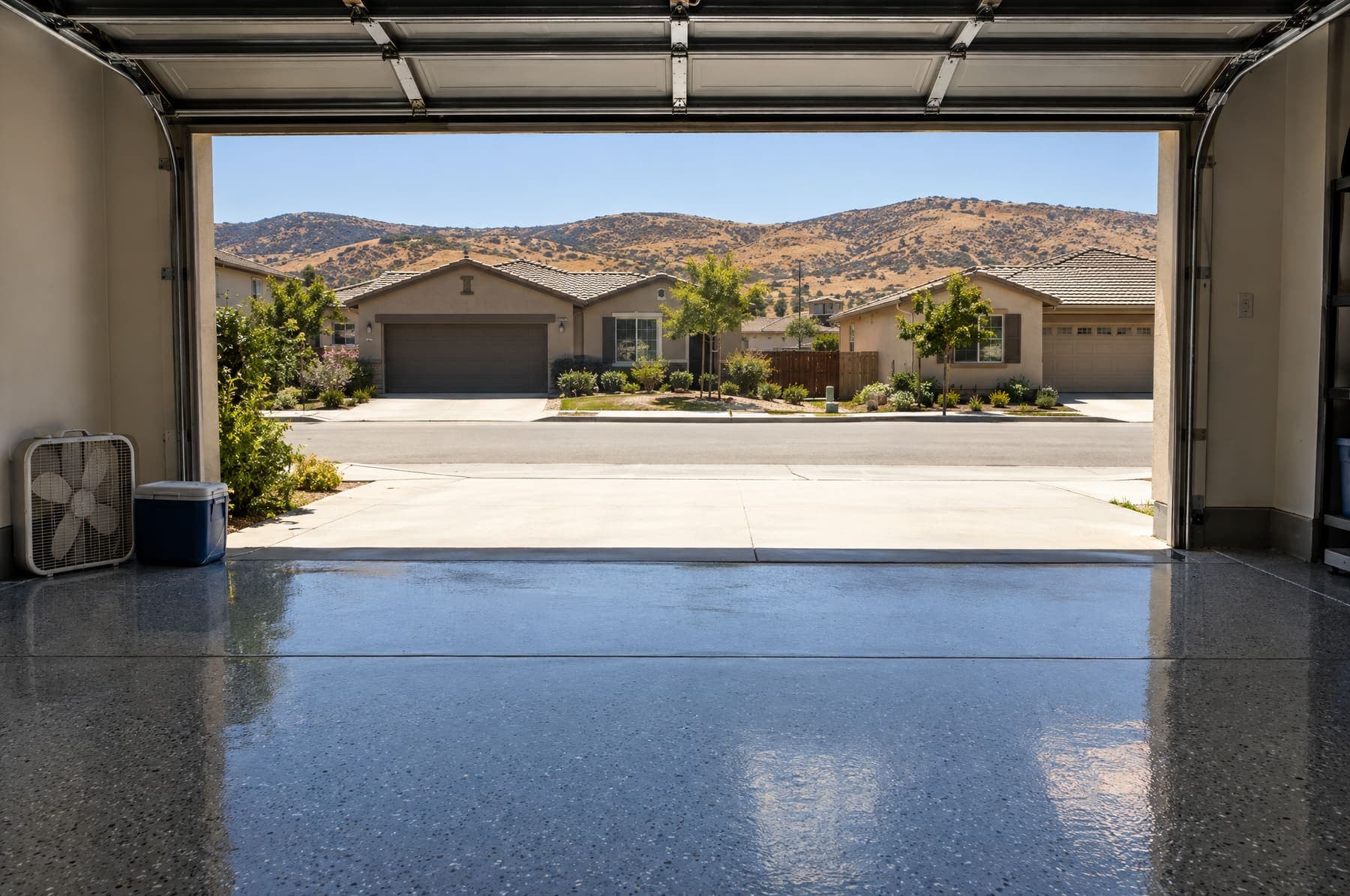 Open garage with a glossy gray flake floor facing a sunny inland street and dry golden hills