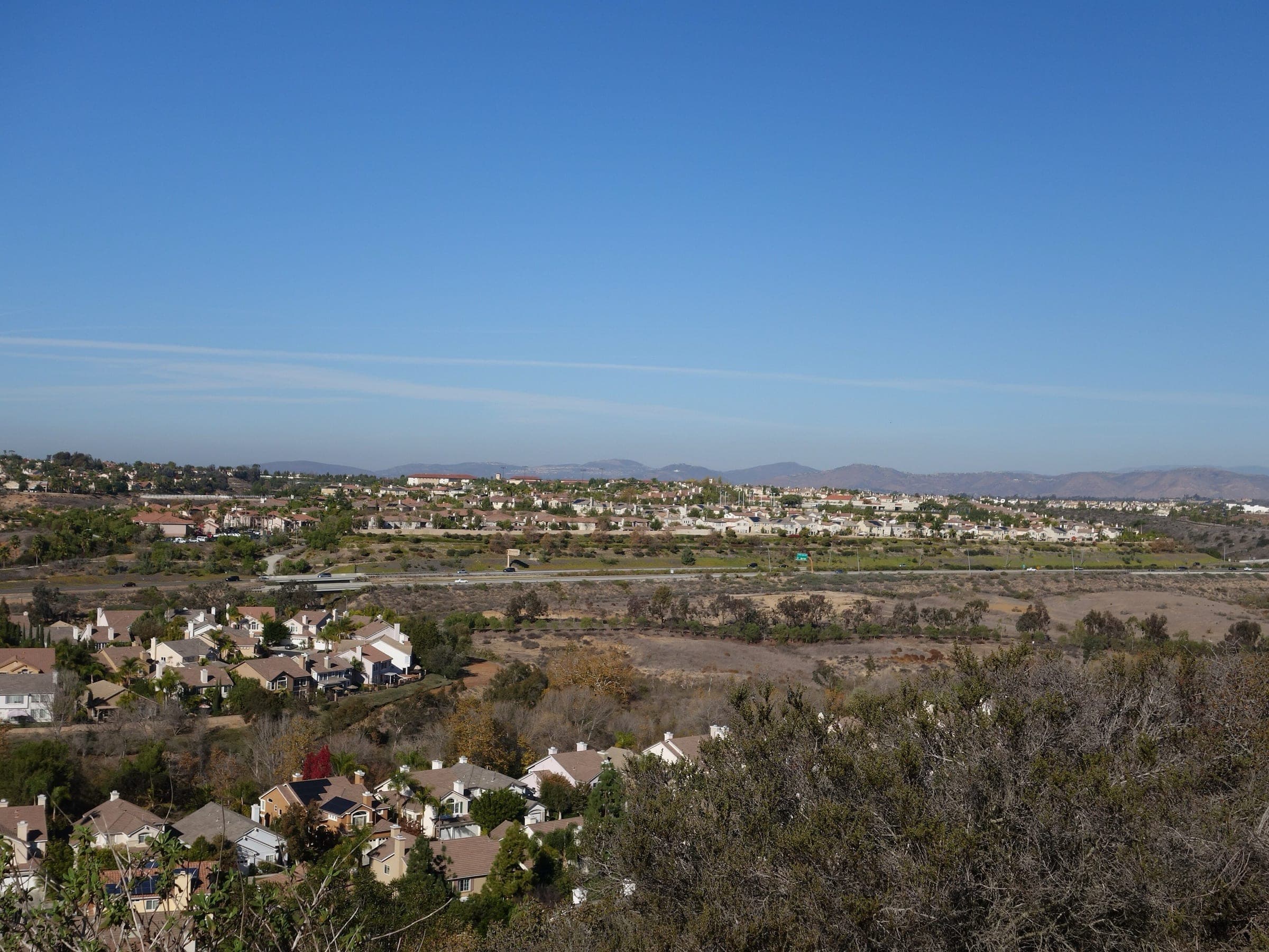 Carmel Valley neighborhoods above a chaparral-covered canyon, with inland mountains on the horizon