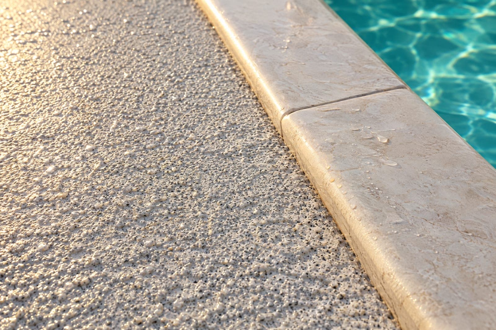 Close-up of a knockdown pool deck texture meeting smooth pool coping